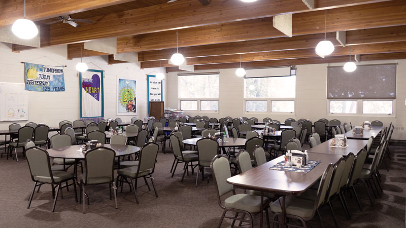 Fellowship hall great room with round tables and chairs facing windows.